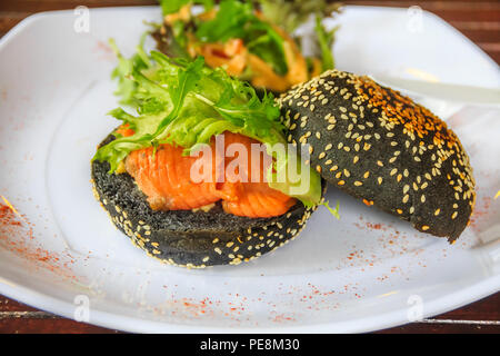 Lachs und ei Sandwich auf einem getoasteten Burgerbrötchen mit Holzkohle Sesamsamen in Singapur auf einem Teller mit Paprika eingerichtet Stockfoto