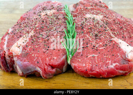 Gepfeffert raw Rib Eye Steaks mit Rosmarin auf einem hölzernen Schneidebrett mit einer geringen Tiefenschärfe Stockfoto