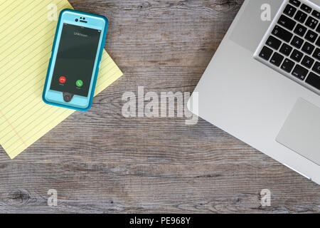 Flach, Holz- Tisch mit Laptop, gelb Legal Pad und ein smart phone mit unbekannter Anrufer. Stockfoto