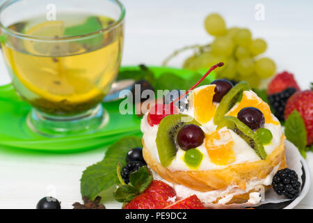 Frisch gebackenes Törtchen mit sortierten Obst und Sahne serviert mit einer Tasse heißen erfrischenden Tee und eine Auswahl an frischem Obst Stockfoto