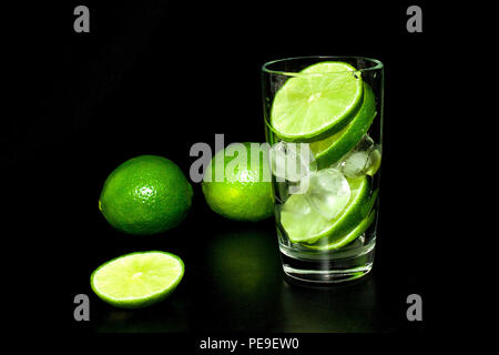 Glas mit Eis und frischen Reifen grün Limes auf schwarzem Hintergrund. Vorbereitung der Limonade. Mojito Cocktail. Frühling und Sommer erfrischende Getränke und Co Stockfoto