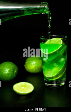 Erfrischende Sommer und Getränke Konzept. Strom der kalte Limonade Wasser aus einer Flasche in ein Glas kaltes Getränk mit Eis und frischen Reifen Scheibe g gegossen Stockfoto