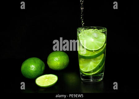 Kalte detox Wasser mit Eis und frischen Reifen Scheibe grün Limes auf schwarzem Hintergrund. Erfrischende Sommer und Getränke Konzept. Kalte detox Wasser mit Eis und Stockfoto