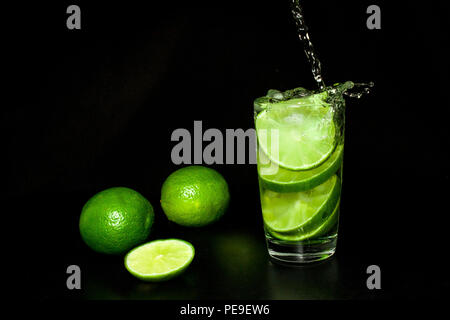 Erfrischende Sommer und Getränke Konzept. Glas kaltes Getränk mit Eis und frischen Reifen Scheibe grün Limes auf schwarzem Hintergrund. Hausgemachte Limonade. Mojito Stockfoto