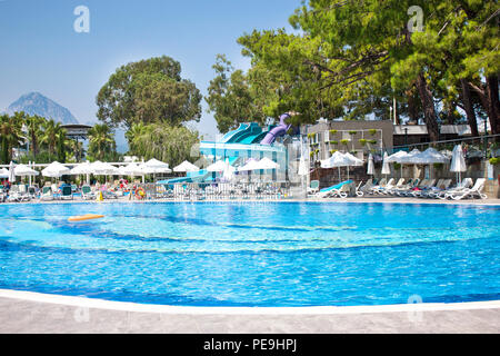 Großer Pool mit Wasserrutschen, unter blauem Himmel. Berge und Kiefern im Hintergrund Stockfoto