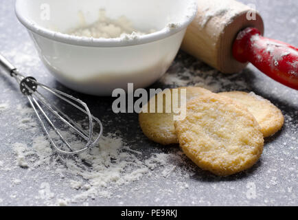 Scharfe Sugar Cookies werden von Mehl und Kochutensilien auf dieser dunklen Grau Arbeitsplatte umgeben. Die Cookies haben eine fantastische Textur, die Ansicht ermöglicht Stockfoto