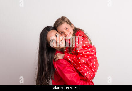 Portrait eines glücklichen Mutter Holding ein kleines Mädchen mit roten Anorak im Studio. Stockfoto