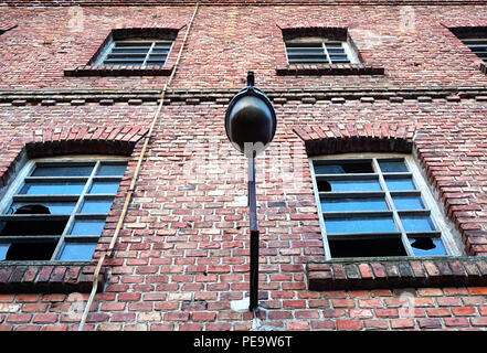 Industrieruinen details. Gebäude mit Fenstern mit Glasscherben und Lampe auf der Fassade aus rotem Ziegelstein auf der alten Fabrik Stockfoto