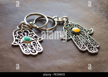 Zwei Schlüsselanhänger in Form von Fatima Hand auf braunem Hintergrund. Altes Symbol und traditionellen moderne touristische Souvenir von Tunesien. Stockfoto