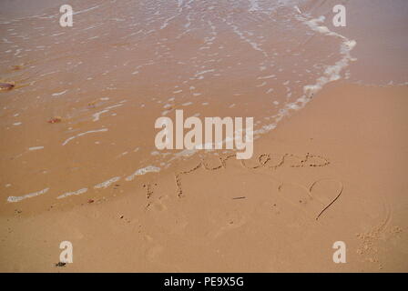 Verschwinden Wort "Glück" wunderschön handschriftlich auf dem roten Sand auf einem Strand mit einer Welle, die in der linken oberen Ecke, Prince Edward Island Stockfoto