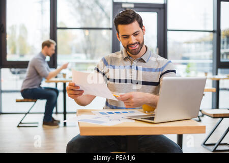 Meine Arbeit. Angenehm erfreut, netter Mann am Tisch sitzen und halten eine Zeichnung bei Tablet Bildschirm schaut Stockfoto