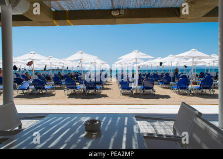 Sandstrand in der Nähe von Aqaba mit Sonnenschirmen, Board-Walk und Touristen. Voula Strand, Glyfada, Griechenland. Stockfoto