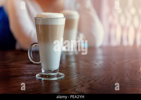 Latte Macchiato trinken im großen Glas hautnah. Kaffee sahne Cappuccino am Tisch im Café. Aufwachen, morgen sucht Konzept Stockfoto