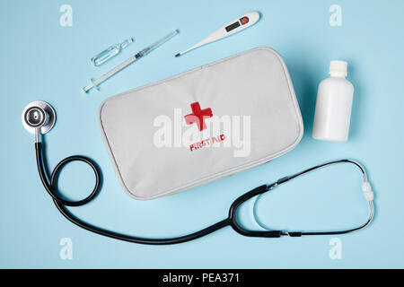 Blick von oben auf die weiße Erste-Hilfe-Tasche mit Stethoskop und Medikamenten auf das blaue Fläche Stockfoto