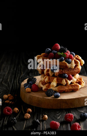 Stapel von belgische Waffeln mit Beeren auf Holz Schneidebrett auf Schwarz Stockfoto
