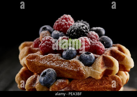 Nahaufnahme der leckere Belgische Waffeln mit Beeren mit Zucker Pulver verschüttete auf Schwarz Stockfoto