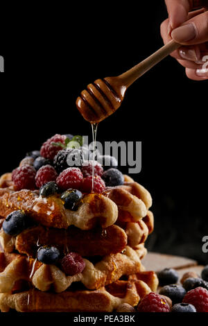 7/8 Schuß von Frau Honig Gießen auf Stapel von belgischen Waffeln auf Schwarz Stockfoto