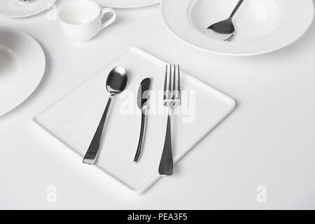 Selektiver Fokus der verschiedenen Teller, Tasse, Gabel, Messer und Löffel auf weißen Tisch Stockfoto