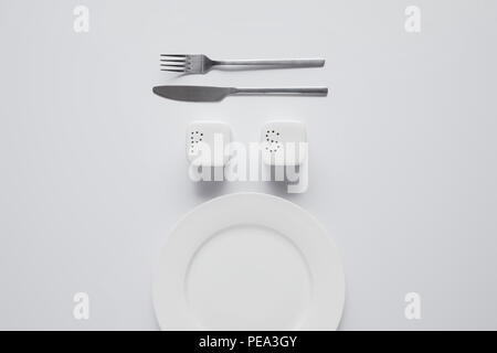 Ansicht von oben angeordnet, Teller, Gabel, Messer, Salzfass und Pfeffer caster auf weißer Tisch, minimalistisches Konzept