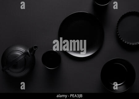 Blick von oben auf die schwarzen Teekanne, Teller, Schüssel, Tassen und Auflaufform auf schwarz Tabelle Stockfoto