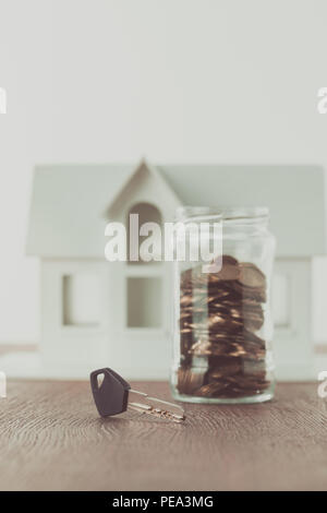 Schlüssel in der Nähe von Glas Münzen auf der Tischplatte mit kleinen Haus auf Hintergrund, Konzept speichern Stockfoto