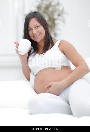 Glücklich schwanger Frau trinkt Milch im Wohnzimmer sitzen. Stockfoto