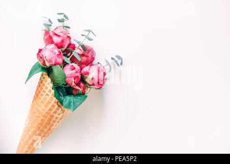 Kreative minimalistische Komposition mit Waffel Kegel mit Rosen und Eukalyptus innen auf weißem Hintergrund. Das Konzept von Geschenk- und Feier. Stockfoto