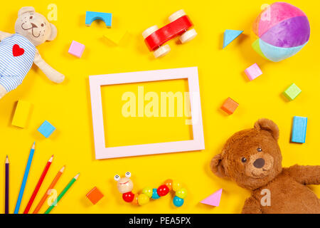 Baby Kinder Spielzeug Hintergrund mit leeren Rahmen wooden Stofftiere und Buntstifte auf gelben Hintergrund. Ansicht von oben Stockfoto