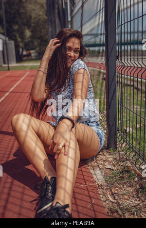 Ein schönes Lächeln Asian Girl posiert und Spaß im Freien. Sie sitzt auf der Stadt Basketballplatz an einem schönen Sommertag. Auf der Suche bei ca Stockfoto