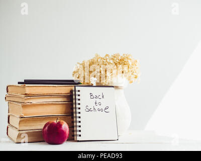 Vintage Bücher, Bleistifte, Notizblock mit einem handschriftlichen Aufschrift und einen Apfel auf einer hölzernen, weißer Tisch. Nahaufnahme, isoliert. Zurück zur Schule Stockfoto