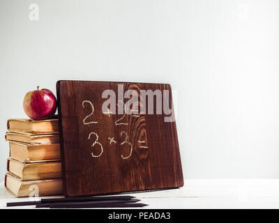 Vintage Books, alte Uhr, Bleistifte, roten Apfel und Tafel mit einem handschriftlich verfassten Inschrift auf einem Holz-, weißer Tisch. Nahaufnahme, isoliert. Zurück zu schoo Stockfoto