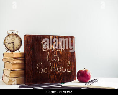 Vintage Books, alte Uhr, Bleistifte, roten Apfel und Tafel mit einem handschriftlich verfassten Inschrift auf einem Holz-, weißer Tisch. Nahaufnahme, isoliert. Zurück zu schoo Stockfoto