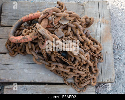 Rostige Kette mit Karabinerhaken Verlegung auf verwitterte Kantholz auf sandigem Untergrund. Stockfoto