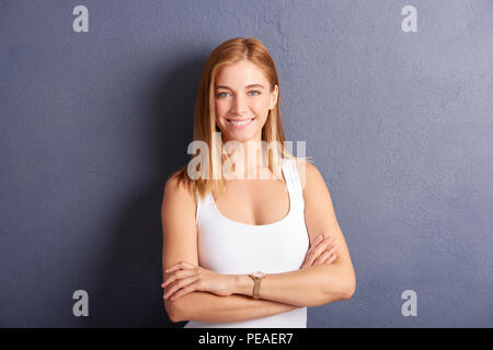 Porträt der schönen jungen Frau mit gekreuzten Armen gegen an der grauen Wand posieren. Stockfoto