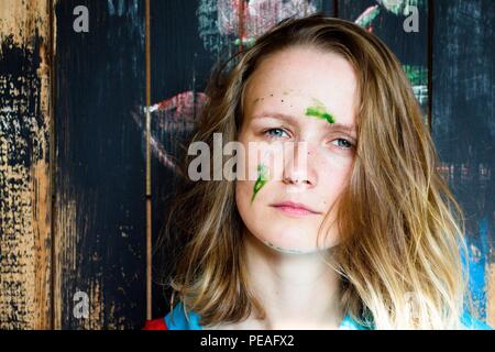 Schöne und junge Mädchen steht auf einer hölzernen Wand Hintergrund, die mit schwarzem Lack lackiert ist. Das Gesicht des Mädchens ist mit grüner Farbe gefärbt. Stockfoto