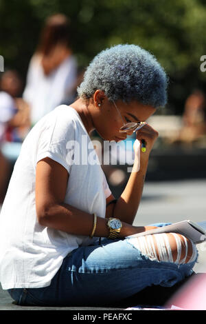 NEW YORK, NY-SEPTEMBER 02: junge schwarze Frau Studium ein Buch während der Sitzung in Washington Square Park, Manhattan am 2. September 2016 in New York, USA Stockfoto