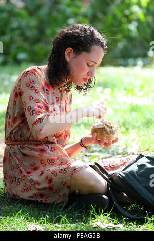 NEW YORK, NY - 05. SEPTEMBER: junge weiße Frau isst Mittag beim Sitzen auf Gras im Washington Square Park, Manhattan am 5. September 2016 in New York Stockfoto