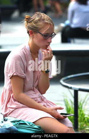 NEW YORK, NY - 05. SEPTEMBER: junge weiße Frau überprüft Ihr Telefon während der Sitzung in Washington Square Park, Manhattan am 5. September 2016 in New York, U Stockfoto