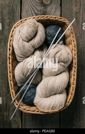Ansicht von oben in Beige und Grau Strickgarn wit Stricknadeln in Weidenkorb auf hölzernen Hintergrund Stockfoto