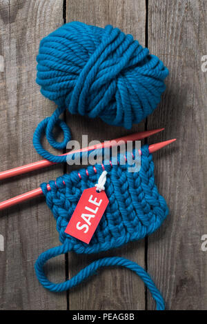 Blick von oben auf die blaue Stricknadeln, blaue Garn Kugel und Verkauf Tag auf hölzernen Hintergrund Stockfoto