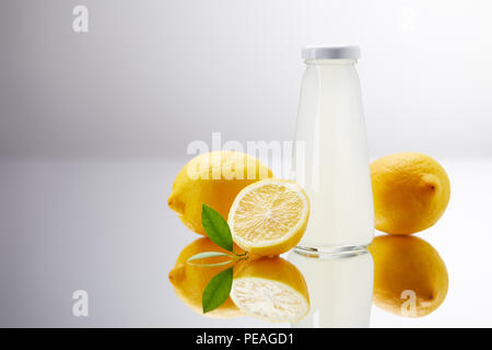 Glas Flasche leckeren Limonade mit Zitronen auf spiegelnden Oberfläche und auf Grau Stockfoto