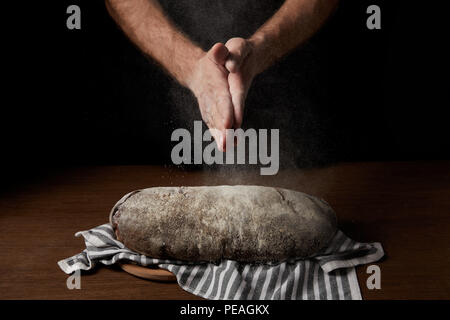 7/8 shot der männlichen Bäcker Händeklatschen mit Mehl über Brot auf Sack Stockfoto