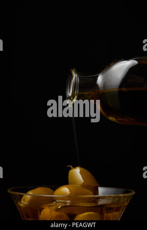 Aromatisches Olivenöl in Schüssel mit Oliven aus Flasche isoliert auf schwarz Gießen Stockfoto