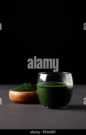 Frische spirulina Drink in Glas und spirulina Pulver in Houten auf schwarzem Hintergrund Stockfoto