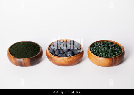 Holz- angeordneten Schalen mit Blaubeeren, Spirulina Tabletten und spirulina Pulver auf weißem Hintergrund Stockfoto