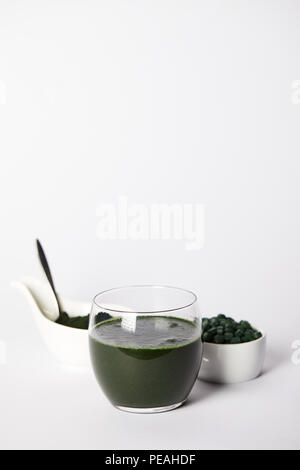 Frische spirulina Drink in Glas, Löffel, spirulina Pulver, Spirulina Tabletten in Schalen auf grauem Hintergrund Stockfoto