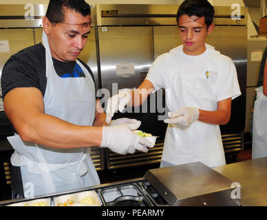 Master Sgt. Roy Garza, 149 Operationen Mitglied der Gruppe, und Tyler Larouche, 14, eine Mikrowelle - sichere Lebensmittel Fach auf ein Förderband für Verpackungen bei einer Mahlzeiten auf Rädern Küche in San Antonio, Texas, November 23, 2015. Verschiedene Mitglieder der Gruppe von Joint Base San Antonio freiwillig zu packen und Lebensmittel in Vorbereitung für den beschäftigten Thanksgiving Woche dienen. Stockfoto