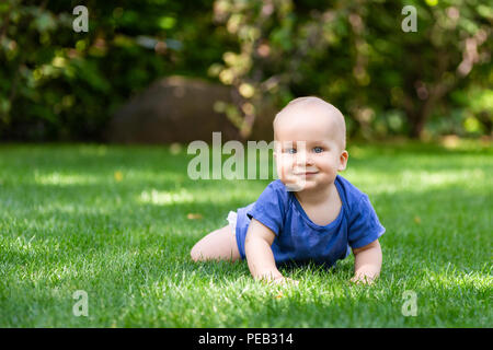 Süße kleine Blonde baby boy Kriechen auf frische grüne Gras. Kind Spaß machen erste Schritte auf natürlichem Rasen gemäht. Gesunde und glückliche Kindheit Konzept Stockfoto