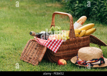 Leckere Früchte und eine Flasche Champagner im Weidenkorb auf grünem Gras im Picnic Stockfoto