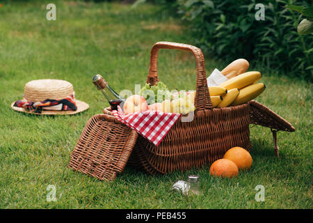 Köstliche Früchte und eine Flasche Champagner im Weidenkorb auf grünem Gras im Picnic Stockfoto
